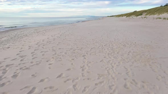 AERIAL: Very Slow Flying Above Sandy Beach with Foot Prints and Seashore on the Side