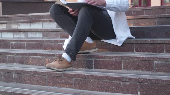 A Medical University Student is Studying Reading Medical Reports Sitting on the Stairs Outside the