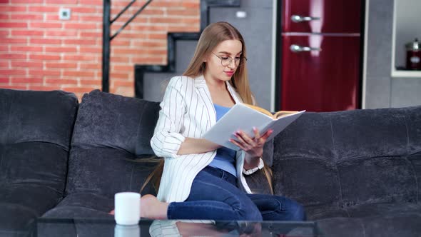 Trendy Smiling Student Young Girl Relaxing Reading Interesting Book at Home Sofa Full Shot