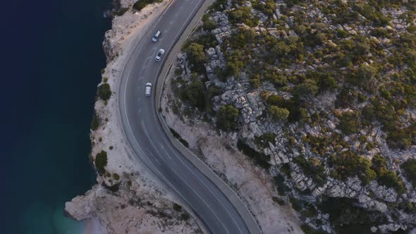 Cars Driving on Coastal Road Through Mountain Rocks and Blue Ocean