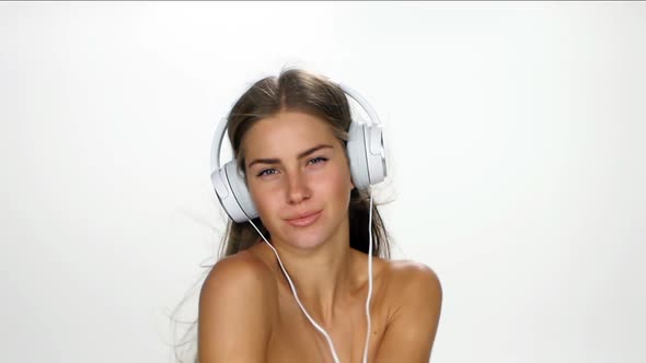 Beautiful Female in Headphones Listening To the Music with Fluttering on the Wind Hair Over White