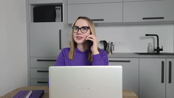 Young Adult Woman in Violet Hoodie Speaks on a Cell Phone and Using Laptop