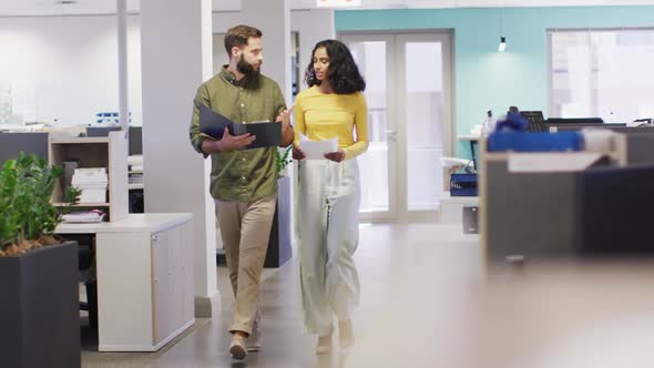 Video of happy diverse businesswoman and businessman walking and talking in office