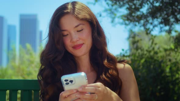 Brunette Typing Message on Phone in Park