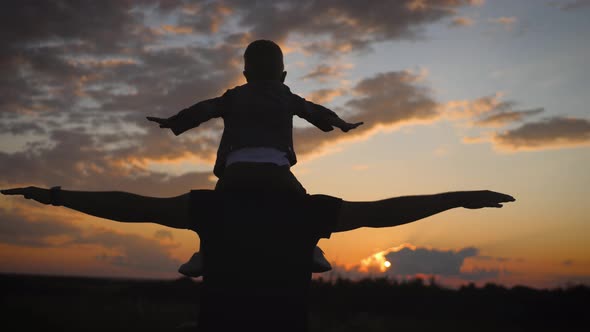 Silhouette Father and Little Son Playing on Meadow. They Rising Up Hands Imitating a Flight at