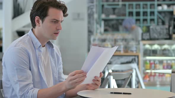 Young Man Reading Documents in Cafe