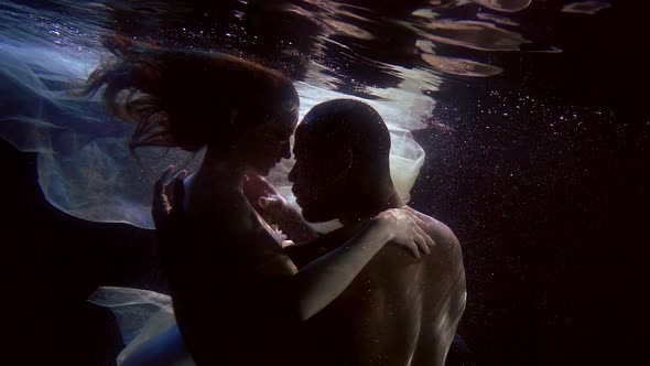 Man and Woman Are Having Sex Underwater in Dark Depth of Pool, Brawny Man Is Embracing Girlfriend