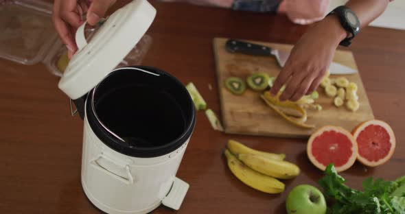 Hands of biracial man composting vegetable waste in kitchen