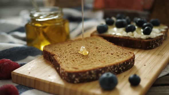 Clear Liquid Honey Pouring on a Piece of a Black Rye Bread. Close Up