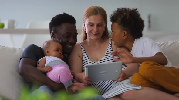 Happy African Interracial Family Parents and Little Children Enjoy Using Tablet Together Sit on Sofa