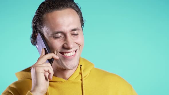 Young man in yellow wear talking on mobile phone on blue background.