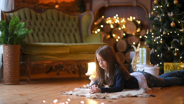 girl lies on the floor against the background of a festive Christmas tree and reads a book.