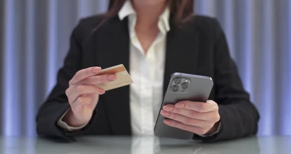 Businesswoman Sitting at the Table and Pays for Purchases Online Using a Smartphone Enters Credit