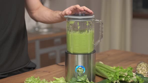 The man turning on blender with a ready-made green smoothie, for better mixing