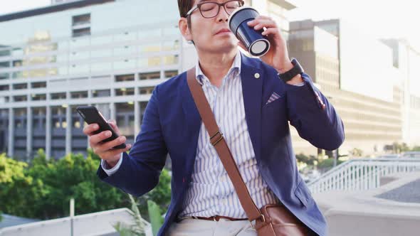 Asian man drinking coffee and using smartphone while sitting on the roof of corporate park