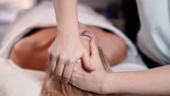 Woman masseur makes face relaxing massage to young beautiful female client blonde and spa treatment