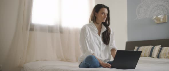 A young woman sitting in bed, thinking about writing something on her laptop