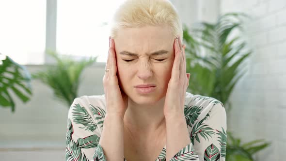 Close Up Young Blond Short Hair Woman with Bun on Her Head is Experiencing Severe Headaches