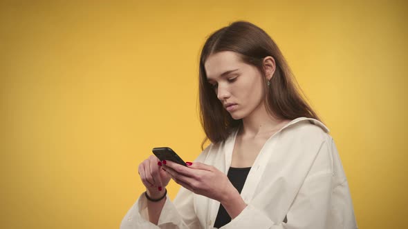 Young Adult Caucasian Woman is Browsing on Her Smart Phone on a Bright Yellow Background