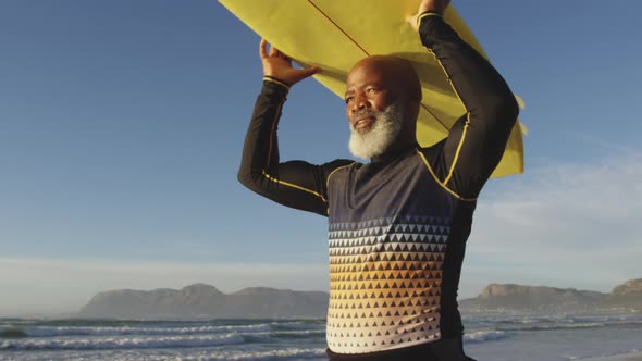 Senior african american man walking with a surfboard on his head at the beach