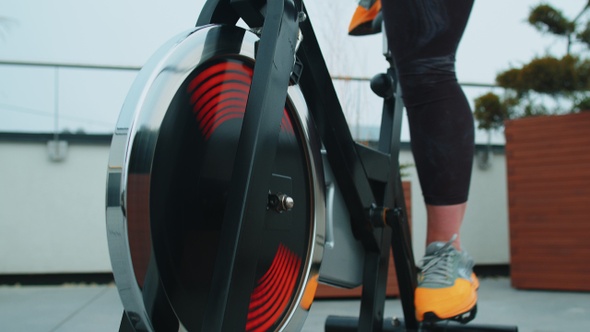 Athletic Girl Performing Aerobic Riding Training Exercises on Cycling Stationary Bike on House Roof