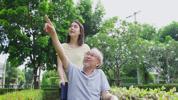 Asian happy Senior retired grandfather on wheelchair enjoy outdoor at  park with his daughter.