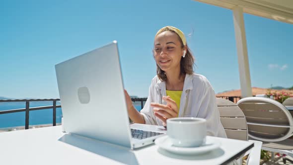 Happy Woman in Earphones Laughing and Speaking with Someone By Laptop Outdoors on Summer Terrace