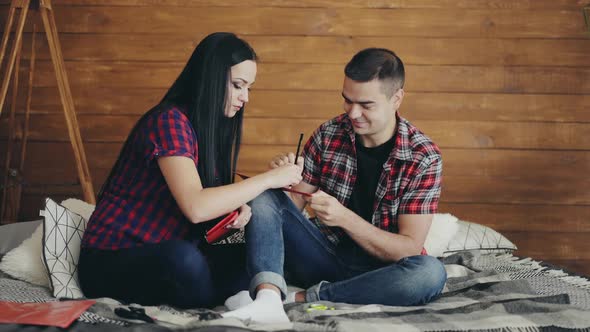 loving couple are sitting on a bed and carving hearts with scissors to Valentine's Day