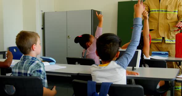 Schoolkids raising hands while male firefighter teaching about fire safety in the classroom 4k