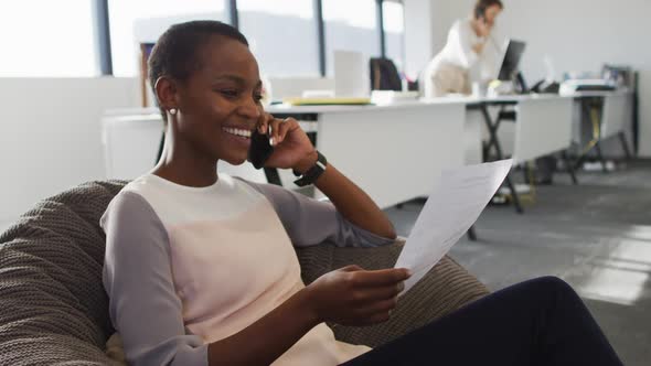 African american businesswoman working in armchair while her coworker having a business call