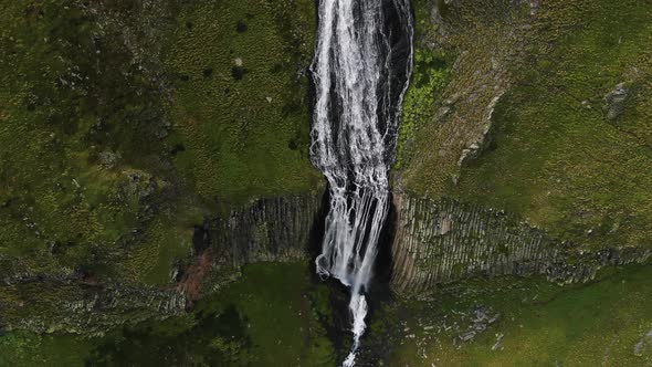 Aerial View of a Fantastic Waterfall in the Mountains Among Rocks and Green Slopes