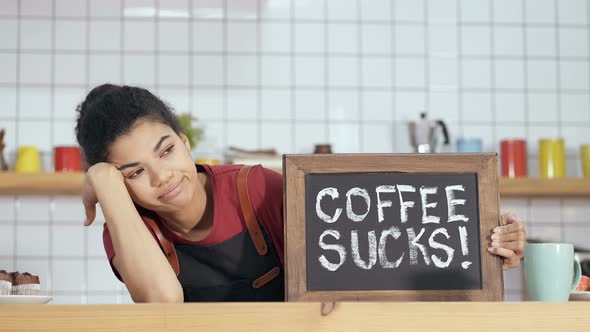 Unhappy barista holding borad with sign "Coffee sucks".