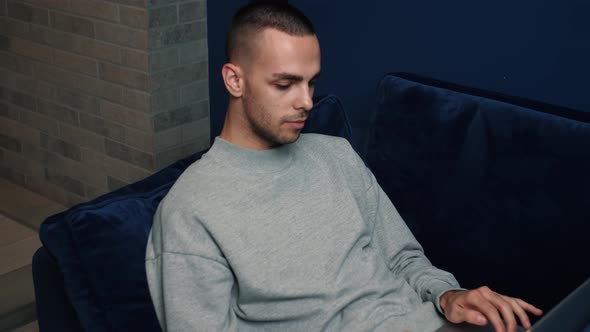 Relaxed Serious Man Student Freelancer Using Laptop Device Leaning on Sofa at Home Office, Focused