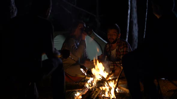 Campers Group Sitting Around Fire Drinking Alcohol and Grilling Sausages, Fun