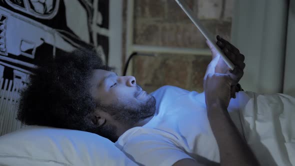 African Man Using Tablet in Bed at Night