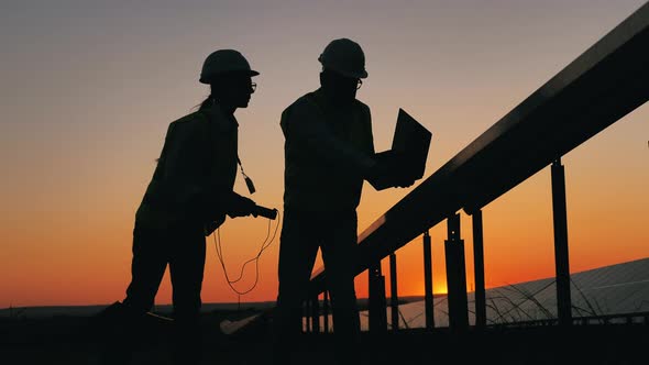 Silhouettes of Two Solar Energy Engineer Checking Solar Panels on a Solar Farm. Alternative, Green