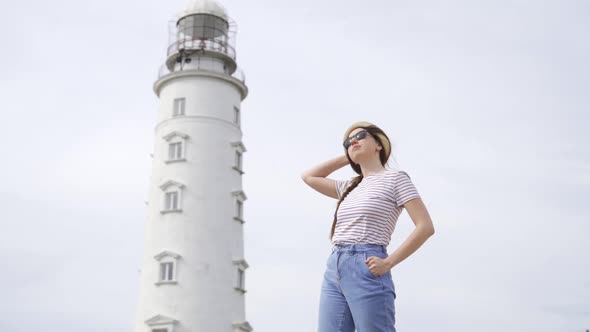 A Beautiful Young Girl Looks at an Lighthouse in a Straw Hat