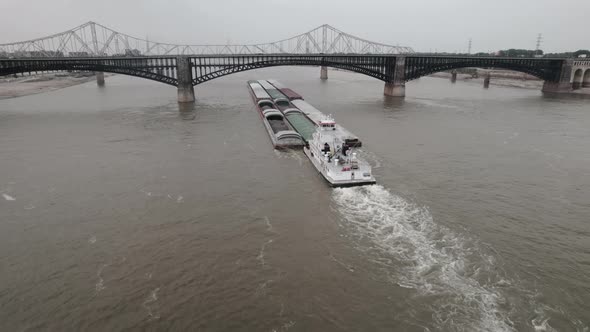 Low aerial parallax of tugboat pushing barges up Mississippi River under bridge