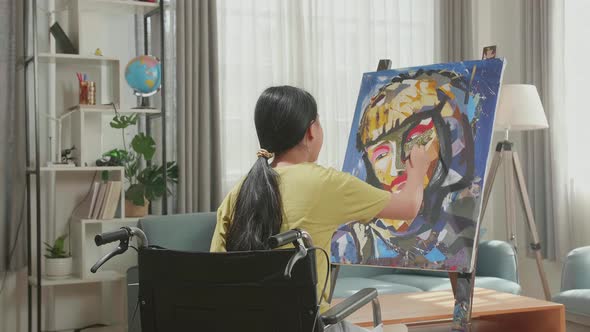 Asian Artist Girl In Wheelchair Holding Paintbrush And Painting A Girl's Face On The Canvas