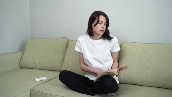 Woman Reading a Book While Sitting on the Couch, Turns on the Cooling Air Conditioner