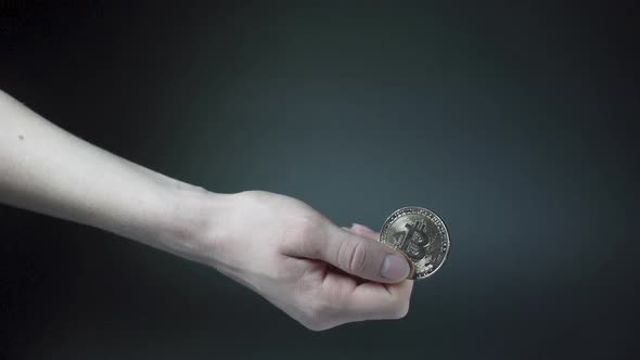 Holding shiny Bitcoin cryptocurrency coin against black background.