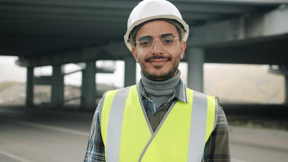 Joyful Arab Guy Wearing Construction Uniform Standing in Urban Building Area Smiling