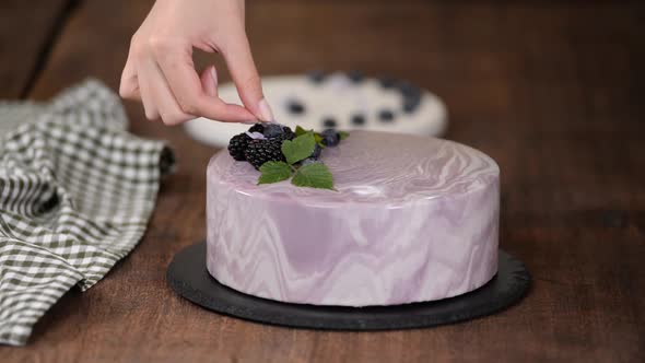 Women's Hands Decorate a Berry Mousse Cake with with Flowers on the Kitchen Table.