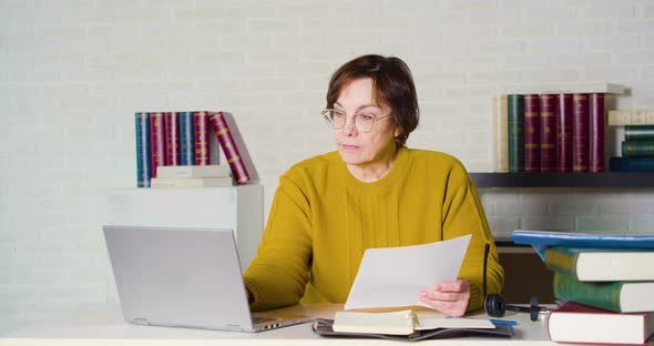 An Elderly Caucasian Woman in Glasses Works in Front of a Laptop Monitor She Checks the Tax Forms