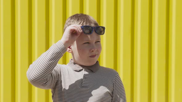 Caucasian Boy Raises Sunglasses and Looks Around Suspiciously Near Yellow Wall