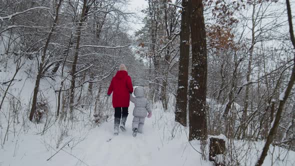 Happy Mom and Her Daughter Running Through the Forest Snow at Sunny Winter Day