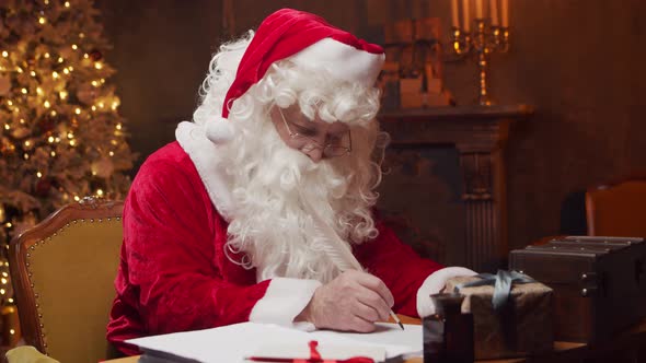Workplace of Santa Claus. Cheerful Santa is working while sitting at the table.