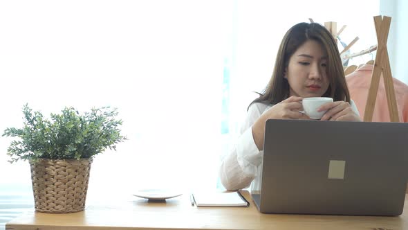 young smiling woman working on laptop while enjoying drinking warm coffee sitting.