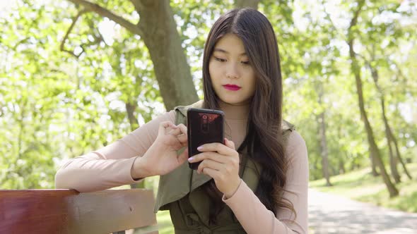 Young Asian Woman Works Smartphone Smile As She Sits Bench Park