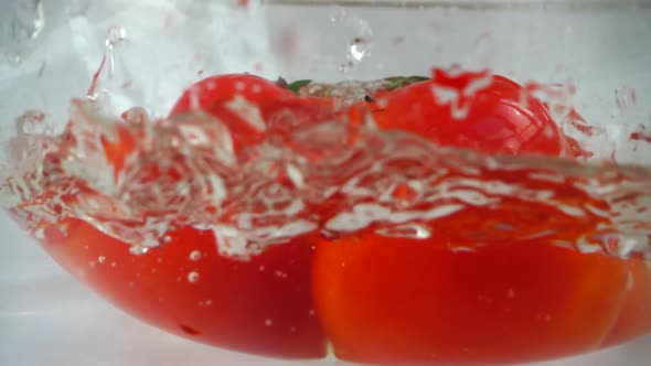 Falling tomatoes in a glass bowl of water. Slow motion.